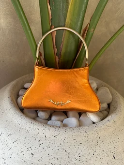 - What the product is: A small metallic gold/orange handbag with a short curved metal handle.
- Apparent audience: Unisex-looking, but styling (compact, metallic finish) leans slightly feminine.
- Notable attributes: Shiny metallic orange/gold leather or faux leather, structured crescent shape with a single metal-tone handle and subtle gold-tone hardware. No visible branding; small decorative metal charm on the front.