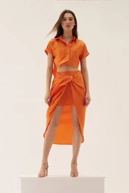 - What it is: A coordinated two-piece set featuring an orange cropped polo-style top and a high-waisted wrap skirt with an asymmetric front tie.
- Intended audience: Women's, based on the model and styling.
- Visible attributes: Bright orange color, lightweight woven fabric, short polo-sleeve cropped top with collar, midriff exposed, wrap skirt with a front knot/tie and high-low drape, matching color, open-toe heels.
Note: Avoids brand identification; describes visible style and materials only.