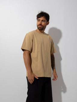 - What the product is: A beige, short-sleeve T-shirt with a relaxed/comfort fit.
- Intended audience: Men (based on model and styling).
- Notable attributes visible: light tan/beige color, loose, boxy cut, crew neck, mid-length sleeves, paired with dark trousers for a casual look. The fabric appears soft and lightweight. No visible branding.