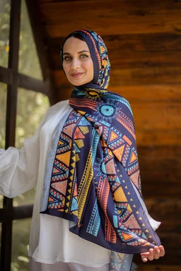 - What the product is: A patterned hijab/shawl worn by a woman, shown styled with a matching wrap around the head and shoulders.
- Apparent audience: Women (female model, modest styling, full-coverage hijab look).
- Notable material, colour, and style attributes: Lightweight fabric with a bold geometric tribal print in navy, blue, orange, yellow, and white. The wrap includes a large scarf draped over the shoulder and a matching bonnet-style headscarf, creating a coordinated, vibrant, geometric design.