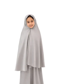 A children’s two-piece modest outfit consisting of a hijab-style cape over a matching long skirt. Intended for girls, judged from the small model and styling. Notable features: light grey color, soft, flowing fabric with a cape-like overlayer and full-coverage silhouette.