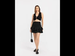 - What the product is: A two-piece black outfit featuring a sleeveless crop top with a front knot and a high-waisted, ruffled mini skirt. 
- Apparent audience: Women, judged from the fitted crop top, feminine ruffle skirt, and styling.
- Notable attributes: Solid black color, cropped top with a cut-out/knotted detail, tiered ruffled mini skirt, paired with black accessories (small handbag and flat shoes). Style is chic and playful, suited for warm-weather or nightlife occasions.