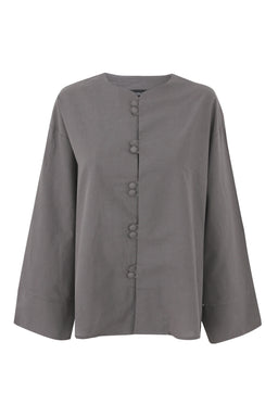 A light grey, long-sleeve button-up top with a mandarin collar. The styling and cut suggest a unisex or women’s relaxed fit, shown with wide, slightly flared sleeves. Notable details include a row of fabric-covered buttons down the front and a smooth, matte linen-like fabric in a muted grey tone.