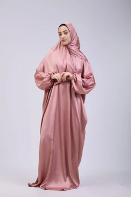 A full-length prayer dress made from smooth satin in pastel pink. The look is modest with a matching hijab and long, loose sleeves, suitable for women; the fabric appears glossy satin with a soft drape and a single, soft gathered detail at the chest. Clean, unembellished styling emphasizes a plain, elegant pastel pink colour and flowing silhouette.