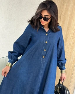 - A knee-to-ankle length denim dress with a relaxed fit and a shirt collar. It features long puff sleeves gathered at the cuffs and a row of large button closures down the front.
- Intended audience: women's fashion.
- Notable attributes: medium-dark blue denim fabric, oversized/loose silhouette, cuffed sleeves with gathered elastic at wrists, gold-tone button details, and a minimalist polo-style placket.