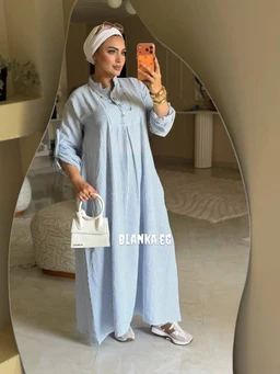 - What the product is: A light blue, ankle-length, striped shirt dress with a relaxed, modest cut.
- Audience: Women, styled for a feminine, modest summer look.
- Notable attributes: Soft, breathable fabric with a vertical stripe pattern; button-front placket, long sleeves that can be rolled; collar neckline; paired with a white head wrap, white handbag, and white sneakers for a casual yet elegant summer vibe. The dress appears flowy and comfortable for warm weather.