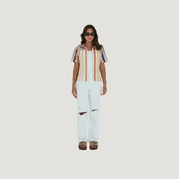 A short-sleeve casual shirt featuring vertical stripe detailing in warm, pastel tones. The model appears to be a woman, suggesting a women’s fit, paired with white distressed straight-leg jeans and platform sandals for a relaxed, boho-chic look. Notable materials and attributes visible include a lightweight fabric with striped color blocks, a button-front placket, and trimmed sleeves.