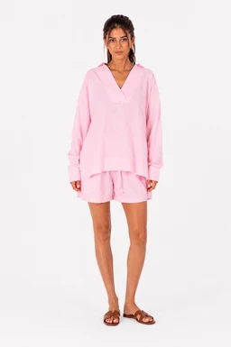 - A blush pink linen pajama set displayed on a female model. The outfit includes a long-sleeve, V-neck top with a relaxed fit and matching above-knee shorts, both in a soft, breathable linen fabric.
- Audience: women (unambiguous from the model and styling).
- Notable attributes: light pink blush color, linen material, oversized top with a V-neck, long sleeves, and loose shorts with a casual, loungewear silhouette. The model wears flat sandals, reinforcing a relaxed, bedroom-to-beach lounge vibe.
