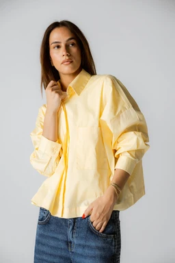 A light yellow shirt with a relaxed, oversized silhouette. The model appears to be a woman, wearing the shirt with long puff sleeves and a classic collar for a casual yet polished look; the color shown is a soft pastel yellow, with a slightly crinkled texture. Notable features include the generous sleeve volume, button-front design, and a single chest pocket; the fabric appears lightweight and breathable, suitable for a casual or smart-casual outfit.