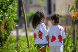 - What the product is: A pair of matching white short-sleeve T-shirts featuring large red heart-shaped graphics on the back, shown on two young girls.
- Apparent audience: Girls (and potentially unisex for children) based on the model sizing and styling.
- Notable attributes: White fabric, oversized red heart graphic on the back, casual short-sleeve tee with a relaxed fit, paired with light denim shorts or skirts in the scene. No visible branding.