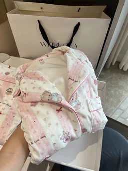 - Product: Soft Teddy Dreams Pajama Set (baby/child-sized loungewear) being held up for display.
- Audience: Intended for children (based on small size, pastel playful prints, and stuffed animal theme).
- Notable attributes: Light pink and white plush quilted fabric with teddy bear motifs; soft, fuzzy texture; full-length top and matching pajama bottoms with pastel print; zipper or button closure visible on the jacket; cozy, pajama-tone styling. Color palette is pinks and whites with small bear illustrations.
