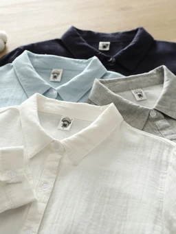 What it is: A display of multiple lightweight polo shirts laid flat, showcasing collared knit knitwear in a row.

Intended audience: Unisex-leaning toward adults; styling and sizing cues suggest a classic polo suitable for men.

Notable attributes: Soft, breathable linen-like or cotton fabric in light neutrals (white, ivory) plus pale blue, heather gray, and navy; short-sleeve, button-front polo with a folded collar and placket.