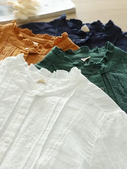 - What the product is: A collection of lightweight, textured blouses or shirts with stand-up collars and button plackets, neatly stacked in multiple colors.
- Apparent audience: Women (judging by the delicate detailing, fitted collars, and colors).
- Notable attributes: Visible textured fabric with pintuck or embroidered detailing, ruffle-like collar, and soft, breathable materials. Color options include white, cream, orange, green, navy, and possibly brown tones. Style: casual yet refined, suitable for everyday wear.