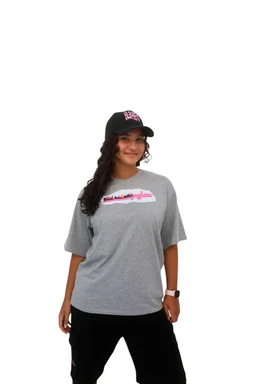- A casual gray T-shirt with a relaxed, oversized fit worn by a female-presenting model. The shirt features a small graphic logo centered on the chest with a pink accent strip and white detailing.
- Intended audience appears as women's/plus-size women based on the model fit and styling. The look is paired with a black cap and black pants for a sporty, streetwear vibe. Notable materials suggest a soft cotton or cotton-blend knit; color is heather gray with a pastel pink-white graphic. Style: short-sleeve crew neck T-shirt with a loose drape.