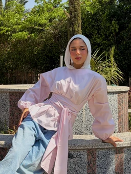 - Product: A light pink poplin top with a wrap design and ample puff sleeves, shown worn by a model.
- Audience: Women (unisex styling could be inferred but presented as women’s fashion).
- Notable attributes: soft pastel pink color, wrap front with a self-tabric belt, voluminous balloon/puff sleeves, high-neck/hood-like neckline, casual yet polished look; fabric appears lightweight poplin.