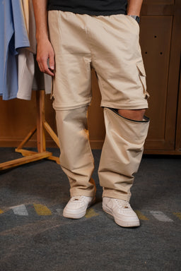 - What the product is: Beige cargo-style pants with reinforced, padded knee sections and a relaxed fit.
- Apparent intended audience: Likely unisex or men's, judging by the cut, length, and styling with white sneakers and a casual top.
- Notable attributes: Beige/khaki color, multiple knee panels with built-in padding or reinforcement, cargo-style pockets, elastic or loose fit at the knees, and white sneakers worn for styling. The fabric appears sturdy and slightly structured.
