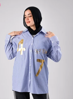 - What the product is: A loose-fit button-down shirt with blue and white stripes, featuring metallic gold appliqué numbers on the front.
- Intended audience: Women's (model styling includes a hijab and feminine fit).
- Notable attributes: Striped cotton or cotton-blend fabric, oversized cut, long sleeves with button cuffs, gold numeral embellishments “4” and “7” on the chest area, classic shirt collar, front button placket.