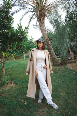 - What the product is: A long, beige wool coat worn open over a light-colored outfits; full-length with wide lapels and a relaxed silhouette.
- Intended audience: Women (model styling, slim fit, mid-calf length coat with tailored yet casual vibe).
- Notable attributes: Material appears wool or wool-blend in a warm beige color; neutral, soft drape; long, oversized coat with wide cuffs, worn over a white knit top and light jeans, finished with sneakers and a cap.