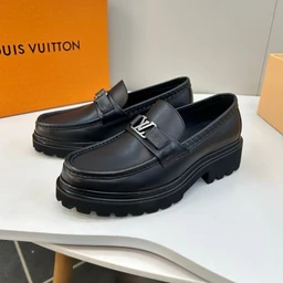 - What it is: A pair of black leather loafers with a thick, lugged sole and a metal LV-style hardware strap across the vamp.
- Intended audience: Unisex or slightly leaning toward adults; the styling and oversized sole suggest a fashion-forward, possibly women’s or unisex urban look.
- Notable attributes: Smooth black leather upper, chunky black rubber sole with deep tread, penny-loafer style strap with metallic accent hardware, minimal stitching visible, classic loafer silhouette. Color is solid black; overall style is chunky, contemporary loafers.