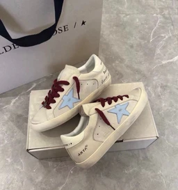- What it is: A pair of casual sneakers in a light beige/cream color with burgundy laces and light blue star patches on the sides. The shoes have a low-top silhouette and a slightly retro style, with visible stitching and a flat rubber sole.
- Intended audience: Unisex-leaning (suitable for both men and women) based on the neutral colorway and generic sneaker design.
- Notable materials and attributes: Light textile/mesh upper with suede-like overlays, burgundy lace-up closure, pale blue star accent, white sole, and subtle text detailing near the heel. Overall style is casual, sporty, and statement-maker due to star motif.