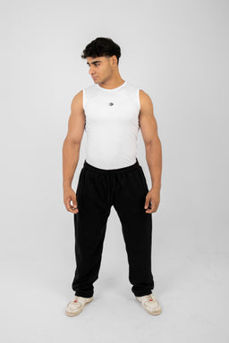 - A white sleeveless compression tank worn by a male model, shown standing with hands at sides.
- Appears aimed at men; cut is tight-fitting sleeveless athletic tank, designed to hug the torso and arms. 
- Notable details: bright white fabric with a small dark emblem on the chest, paired with black jogger-style pants and light-colored sneakers; fabric looks smooth and moisture-wicking, typical of athletic compression wear.