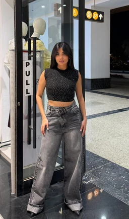 This is a cropped sleeveless crop top in black with small white speckles or embellishments, shown on a female model. The top has a high neckline and a fitted silhouette, paired with high-waisted, wide-leg charcoal gray jeans. The overall styling is casual-chic, suitable for a young adult audience. Notable visible attributes: sleeveless, cropped length, black with subtle texture or sparkle, paired with gray washed denim and a modern streetwear vibe.