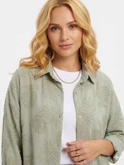 - What it is: A light green/ sage button-front shirt with a subtle floral/leaf embossed pattern worn over a white tee.
- Intended audience: Women (model styling, fit, and accessories suggest women's casual shirt).
- Notable attributes: Soft, breathable fabric with a faint botanical embroidery/texture; long sleeves rolled up; collared neckline; natural, pastel color; relaxed fit.
