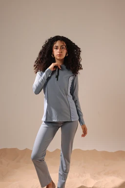 - This is a two-piece athletic loungewear set (long-sleeve top with zipper and matching straight-leg pants) in a light blue/gray tone.
- Intended audience appears to be women, based on the fit and styling, with a slim, model-appropriate silhouette and a cropped-length zip-front top.
- Notable attributes visible: soft, lightweight knit material with a heathered finish, high collar/quarter-zip neckline, long sleeves, and straight-cut pants that reach near the ankles. The overall look is casual, athletic, and suitable for lounge or light workouts.