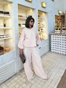 - What it is: A crinkle-set outfit in a light beige tone, consisting of a long-sleeve, loose-fitting top with a round neckline and front placket, paired with wide-leg, relaxed trousers.
- Audience and styling cues: Appears targeted toward women; styled for a casual yet chic, loungewear or resort look with soft, draped silhouettes.
- Notable attributes: Crinkled, textured fabric in pale beige; oversized, billowy sleeves; flowy wide-leg pants; minimal detailing with a simple buttoned top and smooth, coordinated set vibe.