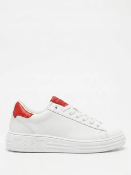 This is a low-cut sneaker with a white leather upper and a white rubber sole. It features a red accent on the heel and a small red detail on the tongue, with white laces and minimal stitching. The style is clean and sporty with a chunky midsole, suitable for a unisex or casual streetwear audience. Visible material attributes include smooth white leather and a textured sole with subtle branding embossed on the side of the midsole.