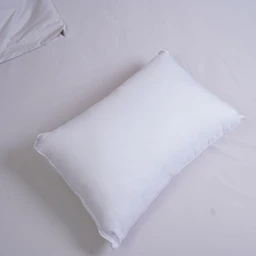 A rectangular white pillow laid on a light-colored bed, photographed from a slight top-down angle. Appears intended for adults (unisex) with a long, plush profile suitable for side or back sleeping; fabric looks smooth and soft, suggesting a microfiber fill and cover. Notable attributes: white microfiber exterior, long rectangular shape, hotel-grade plush appearance, with clean stitching along the edges.