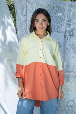 This is a color-block shirt with a soft, oversized silhouette featuring a pale yellow top half and a warm coral-orange bottom half. It appears styled for women, with a relaxed fit, dropped shoulders, long sleeves rolled at the cuffs, and a button-down front. Notable materials appear lightweight and breathable, with a crisp collar and visible seam separation between the two color blocks, giving a two-tone, casual yet polished look.