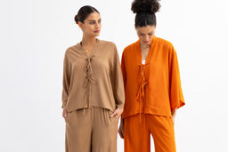 - Product: A two-piece summer loungewear set featuring a tie-front top and matching wide-leg pants. The set is shown in two color options: beige and bright orange.
- Audience and styling: Appears designed for women, with relaxed, oversized silhouettes and casual, comfortable styling suitable for warm weather.
- Notable attributes: Loose, draped top with front ties and a layered, soft fabric; wide-leg pants with an elasticized or relaxed waist. Colors shown are neutral beige and vivid orange. No visible branding.