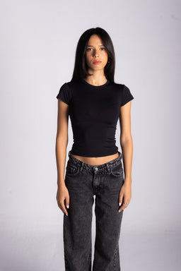 - A black fitted cropped T-shirt with short sleeves on a female model. The shirt is tight and form-fitting, ending just above the waist. 
- Appears designed for women, based on the cut and styling. 
- Notable attributes: solid black color, crew neck, short sleeves, cropped length, paired with high-waisted dark gray/black jeans for a casual, minimalist look.