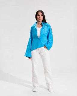 - A turquoise linen shirt worn open over a white top, styled with white wide-leg pants and white sneakers. The shirt has a relaxed, oversized fit with long sleeves and a button-down front; one side is tucked into the pants for a casual look.
- Target audience: unisex or women’s (based on model and styling; appears designed for a women's casual/relaxed fit).
- Notable attributes: bright turquoise color, lightweight linen fabric, long sleeves, oversized/relaxed silhouette, white inner top and pants for contrast.