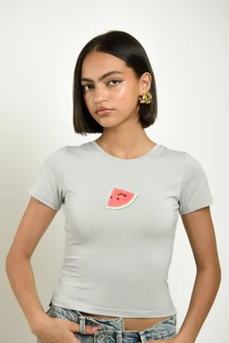 - What the product is: A light gray cropped short-sleeve T-shirt with a small watermelon slice graphic centered on the chest.
- Apparent audience: Women (adult female model), likely unisex style but shown as women’s sizing.
- Notable attributes: Soft knit cotton look, fitted cropped fit, watermelon graphic in pink/green/black, crew neck, plain color background. Material appears lightweight cotton or cotton-blend, with a casual, playful style.