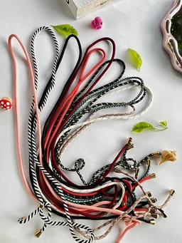 This image shows a collection of colorful cord-style necklaces or lanyards arranged in a loose pile. The apparent audience is unisex, based on the varied colors and simple cord designs. Notable attributes: thin fabric/cord strands in pink, peach, black, red, and striped black/white patterns; some cords have metal tips or small clasps, suggesting adjustable length or wear as accessories. Overall style is casual, lightweight, and versatile for everyday use.