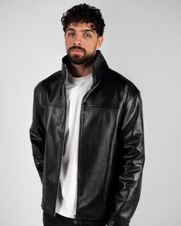 A black leather jacket with a clean, minimal front zipper and a stand-up collar. The model appears as a masculine, adult male, wearing a white T-shirt underneath, suggesting a unisex-to-male styling. Notable details include the smooth leather texture, subtle panels at the shoulders, and a sleek, fitted cut with long sleeves.
