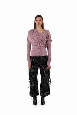 - Product: A mauve draped jersey top with a twisted front detail and long ruched sleeves. The top appears semi-fitted with a wrap-like neckline and a gathered waist, creating soft drapes.

- Audience and styling cues: Designed for a unisex aesthetic but worn here by a female model; overall styling reads edgy-chic with a streetwear influence.

- Visible materials and colors: Soft mauve/rose-pink jersey fabric; matte finish with a draped, crossover front and ruched, long sleeves. The top is paired in the photo with black glossy cargo-style pants and black ankle boots for a bold contrast.