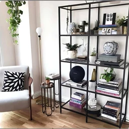 - A tall, black metal-and-glass shelving unit with multiple shelves arranged in a 5-tier grid, placed in a light, modern living room. The unit holds books, decorative objects, small plants, frames, and ceramics, styled with a mix of white, black, and metallic accents.
- Intended audience: unisex (suitable for both men and women; lifestyle/home decor). Notable attributes: matte black metal frame, clear horizontal shelves, varied decor items including books, plants, vases, and framed photos; overall minimalistic, contemporary style. Material emphasis: metal frame with glass or open shelves; color palette dominated by black, white, and neutral tones. Size indicated by title: 120×30×200 cm.