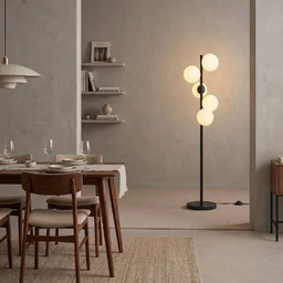 - A floor lamp with a tall, slim black stem and a round base, featuring a vertical arrangement of four glowing globe bulbs. The style is modern/minimal with a warm ambient light, set in a neutral living/dining space.
- Visible materials and colors: metal stem (black) with frosted glass globe shades in warm white; the surrounding decor includes light grey walls, a wooden dining table and chairs, and a beige rug, giving a contemporary, understated look.