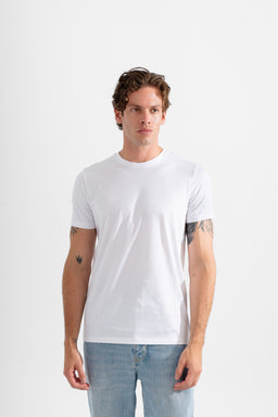 - A plain white crew-neck T-shirt worn by a male model, shown from the waist up in a studio setting with a light background.
- Intended audience: men, based on the model, cut, and styling. Notable attributes: solid white cotton tee, short sleeves, relaxed/standard fit, lightweight fabric, no visible branding or graphics. Material impression suggests soft cotton; color is bright white; style is classic/basic tee.