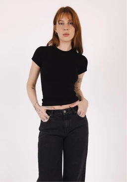 - Product: A fitted half-sleeve top in black.
- Intended audience: Women, based on the model and styling.
- Visible attributes: Short, crew-neck, body-hugging silhouette with cap/short sleeves; solid black fabric; cropped length showing a hint of midriff; paired with high-waisted dark jeans. No visible branding.