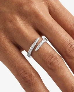 - A double-band ring set, worn on the index finger with two parallel silver bands wrapping around the finger.
- The bands are encrusted with small clear stones (likely crystals or diamonds), giving a sparkling, pavé-inspired look. 
- Visible color attributes: bright silver metal with clear stone accents; style appears modern and elegant with a wrap-around, infinity-like design. Audience judged: women's (based on sizing, finger wearing, and delicate styling). Material impression: silver-toned metal with pavé stones.