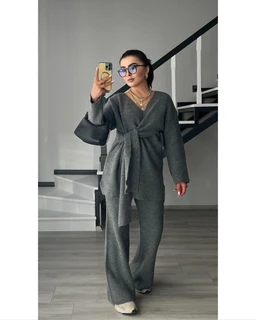 - What it is: A grey knit wrap-set consisting of a long-sleeve cardigan-style wrap top tied at the waist and matching wide-leg knit pants.
- Audience: Women (based on the styling, fit, and accessories).
- Notable attributes: heather grey knit fabric, wrap-front with tie at the waist, relaxed wide-leg pants, coordinated top and bottoms for a cohesive lounge-to-outerwear look; the model carries a dark handbag and wears light-colored footwear, with a casual, modern aesthetic.