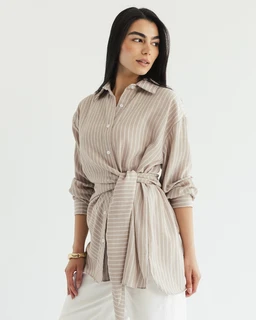This is a lightweight, striped wrap shirt in a soft sand shell tone. It features a classic button-front, a self-tabric belt tied at the waist, and long sleeves with cuffs, styled on a female-presenting model for a relaxed, oversized fit. Visible materials suggest a breathable woven fabric with subtle vertical stripes in beige and off-white.