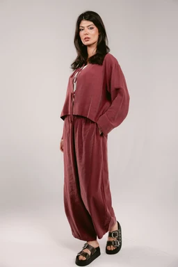 - Product: A burgundy loungewear set consisting of a loose, cropped top with long, voluminous sleeves and matching wide-leg pants. The fabric appears soft and velvety, with a matte finish.
- Audience: Women's; the relaxed fit and draped silhouette suggest feminine styling.
- Notable attributes: Rich burgundy color, velvety texture, oversized top with dropped shoulders, elastic or relaxed waistband on pants, and slide-on sandals as styling. No visible brand or logos.