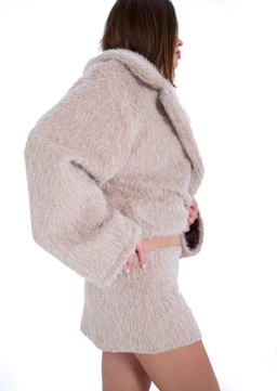 - Product: A light off-white mini skirt paired with a fluffy, matching cropped jacket. The model is shown in a side profile, highlighting a textured, shaggy faux-fur material.
- Audience and styling: Appears styled for a women’s market with a chic, cozy, winter-ready vibe. The look is minimalist and chic, focusing on oversized outerwear and a short skirt silhouette.
- Notable attributes: Material appears to be plush faux-fur or teddy fabric in a soft beige/off-white color; the set emphasizes a cropped jacket and a short, tight-fitting mini skirt with clean lines and a cohesive monochrome color.
