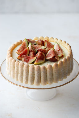 - What the product is: A round dessert cake with a light, fluffy cream filling and a tall scalloped edge, topped with sliced figs.
- Intended audience: Unisex (suitable for everyone; no gender-specific styling).
- Notable attributes: Pale beige outer crumb with vertical ridges, smooth creamy filling, and fresh fig slices arranged on top. TheOverall look is delicate, elegant, and bakery-cake style, with a vanilla-tinged palette.