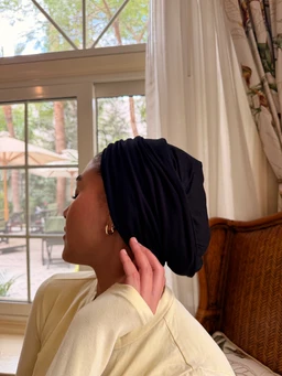 - What it is: A headwrap or turban-style wrap made of black double-layer cotton lycra, worn on the head.
- Intended audience: Women (as shown on a female model).
- Visible attributes: Onyx black color, soft stretch fabric (cotton lycra), gathered/twisted turban style with a loose, draped fit at the back. No branding visible.